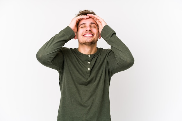 Foto el hombre caucásico rubio joven del pelo rizado aislado ríe alegremente manteniendo las manos en la cabeza. concepto de felicidad