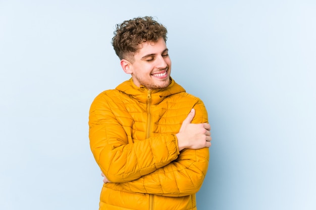 El hombre caucásico rubio joven del pelo rizado aisló abrazos, sonriendo despreocupado y feliz.