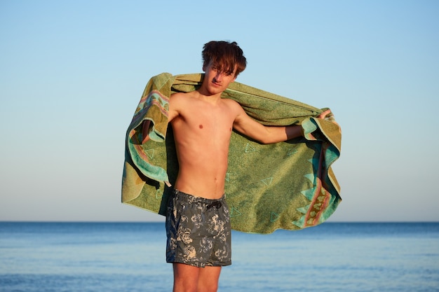 Un hombre caucásico secándose con una toalla verde en una playa con un mar de fondo