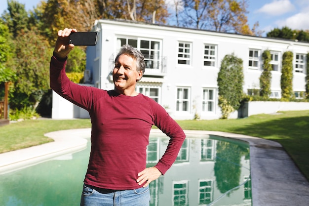 Foto hombre caucásico senior feliz tomando selfies en un jardín soleado. estilo de vida de jubilación de lujo, pasar tiempo en casa.