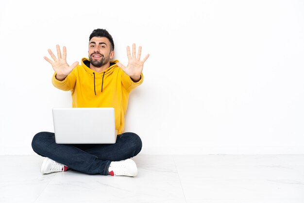 Hombre caucásico sentado en el suelo con su computadora portátil contando diez con los dedos