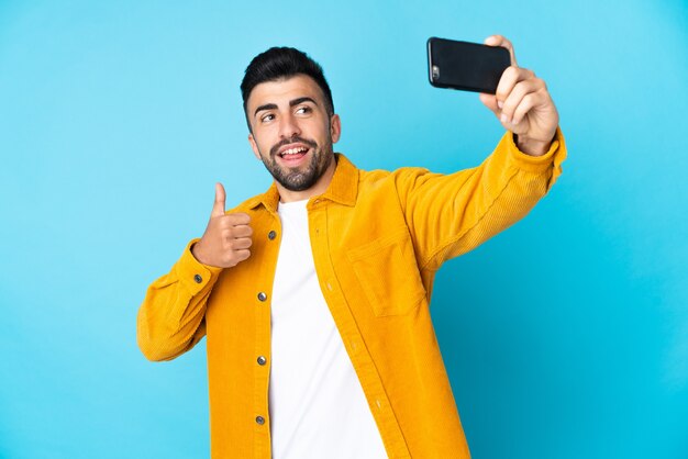 Hombre caucásico sobre fondo azul aislado haciendo un selfie con teléfono móvil