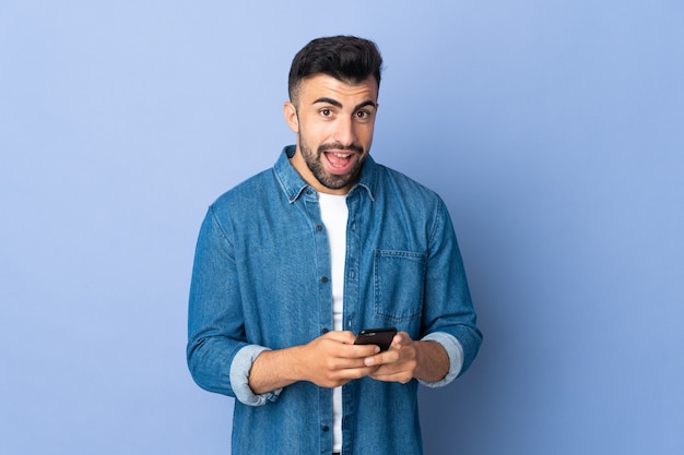 Hombre caucásico sobre pared azul aislada sorprendido y enviando un mensaje