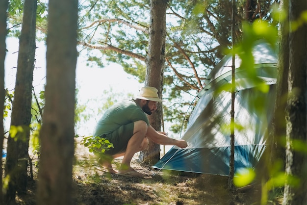 Hombre caucásico con sombrero poniendo una tienda de campaña Concepto de camping familiar