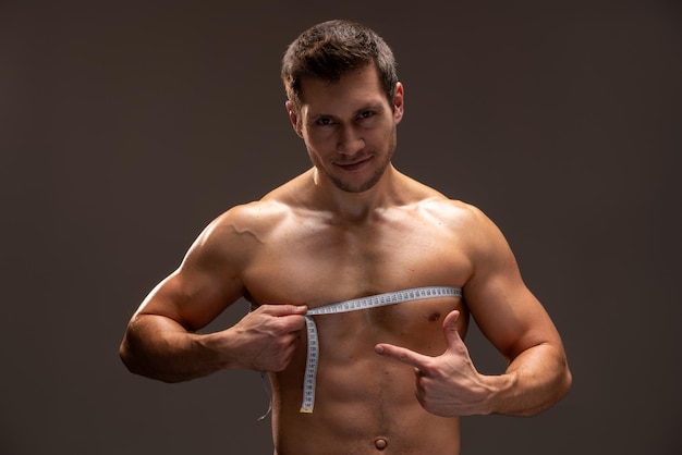 Hombre caucásico sonriente con hermoso cuerpo midiendo su pecho con tipo de medición después de la dieta. Concepto de deporte y dieta.