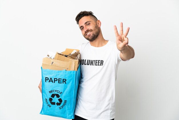 Hombre caucásico sosteniendo una bolsa de reciclaje llena de papel para reciclar aislado sobre fondo blanco feliz y contando tres con los dedos