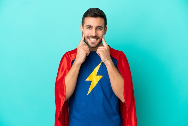 Hombre caucásico de superhéroe aislado sobre fondo azul sonriendo con una expresión feliz y agradable