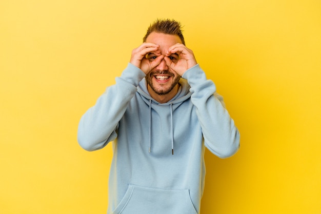 Hombre caucásico tatuado joven aislado sobre fondo amarillo que muestra bien firmar sobre los ojos