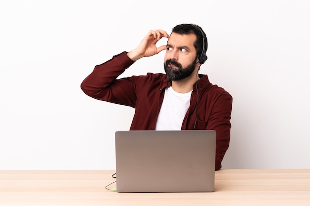 Hombre caucásico de telemarketer que trabaja con un auricular y con una computadora portátil que tiene dudas mientras se rasca la cabeza.