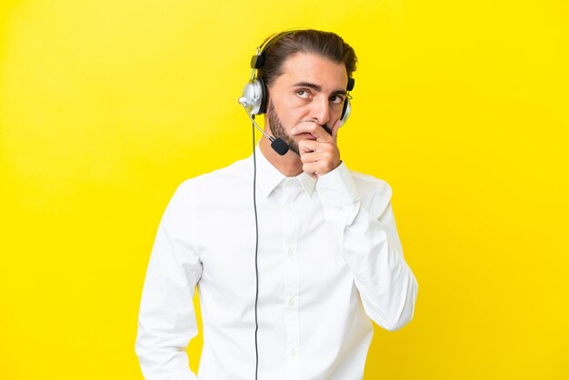 Hombre caucásico de telemarketing que trabaja con un auricular aislado en un fondo amarillo que tiene dudas y con una expresión facial confusa