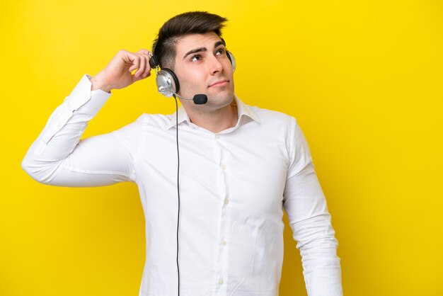 Hombre caucásico de telemarketing que trabaja con un auricular aislado en un fondo amarillo que tiene dudas y con una expresión facial confusa