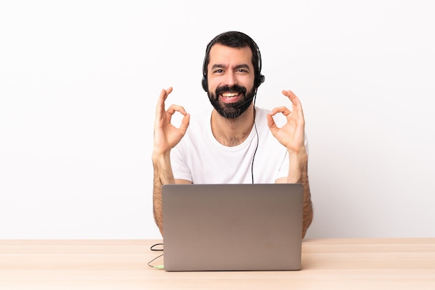 Foto hombre caucásico de telemarketing que trabaja con un auricular y con un ordenador portátil que muestra la muestra aceptable con las dos manos.