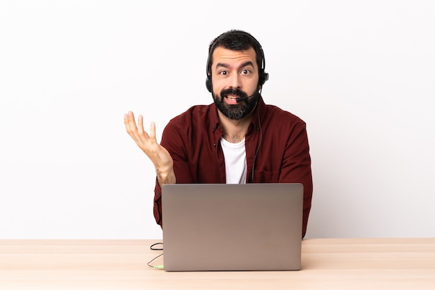 Hombre caucásico de telemarketing que trabaja con un auricular y con un portátil haciendo gesto de dudas.