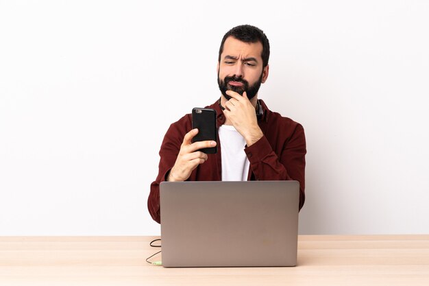 Hombre caucásico de telemarketing que trabaja con un auricular y con un portátil pensando y enviando un mensaje.