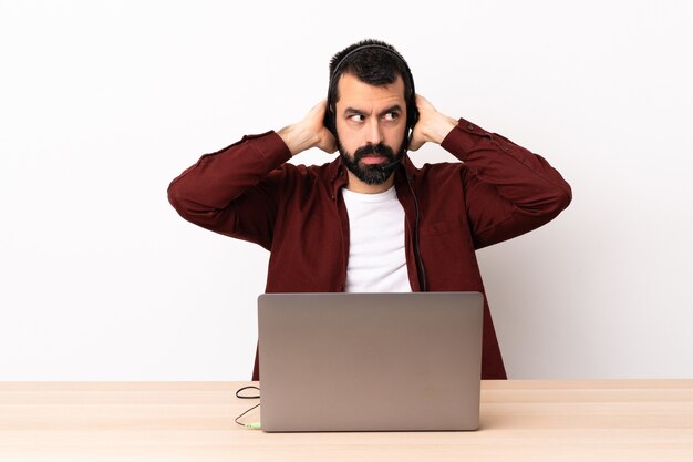 Hombre caucásico de telemercadeo que trabaja con un auricular y con un portátil frustrado y cubriendo los oídos.