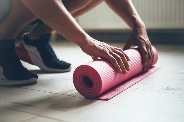 Hombre caucásico terminar de hacer ejercicios está recogiendo su alfombra de yoga del suelo