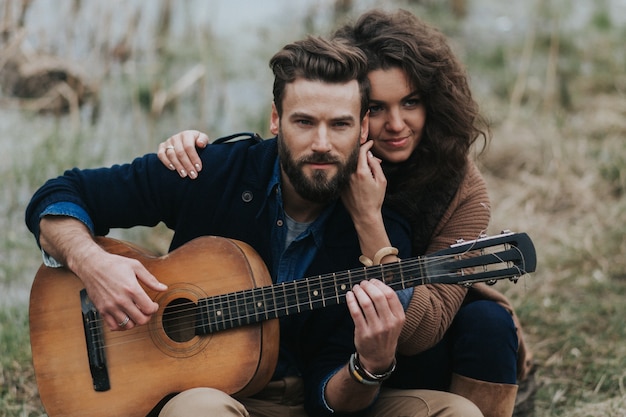 Foto hombre caucásico está tocando la guitarra con la mujer junto al lago