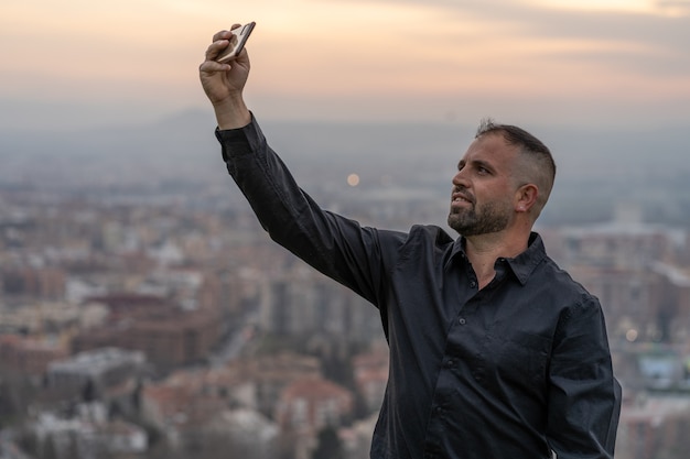 Hombre caucásico tomando un selfie con el teléfono inteligente al atardecer