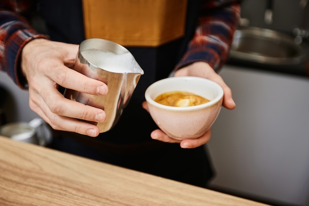 Hombre caucásico vertiendo leche caliente en café