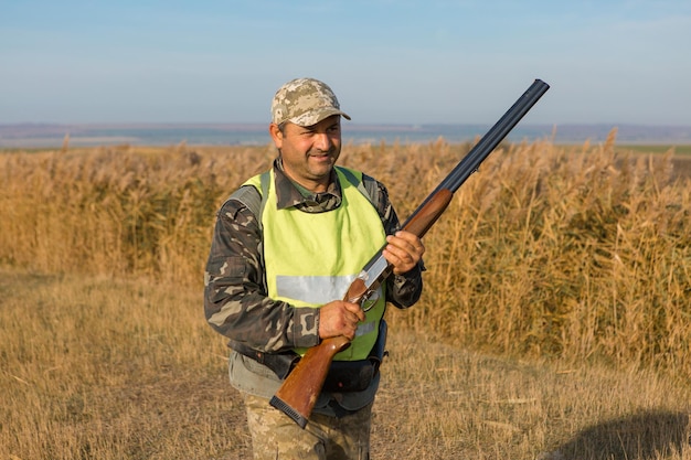 Hombre cazador camuflado con un arma durante la caza en busca de aves silvestres o juego Temporada de caza de otoño