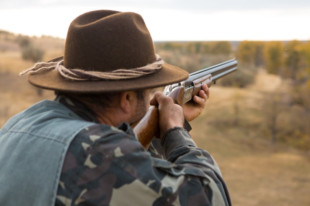 Hombre cazador en camuflaje con una pistola durante la caza en busca de aves silvestres o caza. Temporada de caza de otoño.