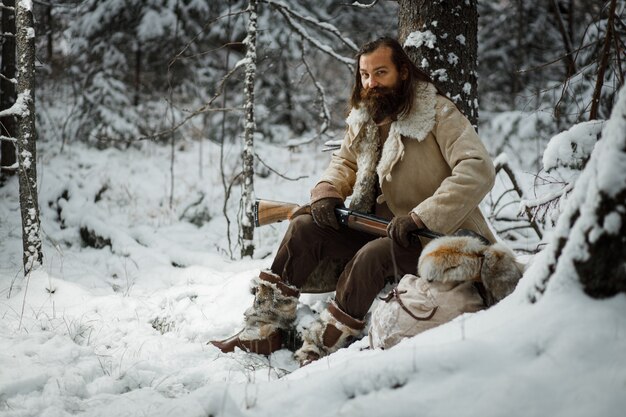 Hombre cazador en invierno cálida ropa vintage con pistola en bosque de invierno