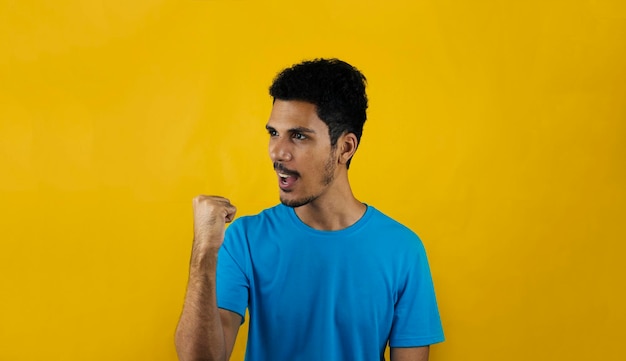 Hombre celebrando aislado sobre fondo amarillo. Hombre negro guapo con camisa azul sobre amarillo.