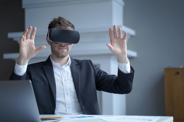 Hombre ceo en gafas de realidad virtual con las manos arriba en el aire en el interior de la oficina en casa