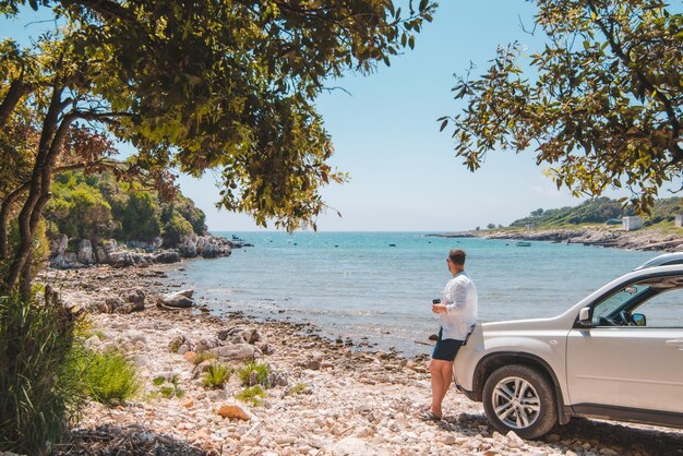 Hombre cerca de un coche todoterreno blanco en la playa de mar de verano