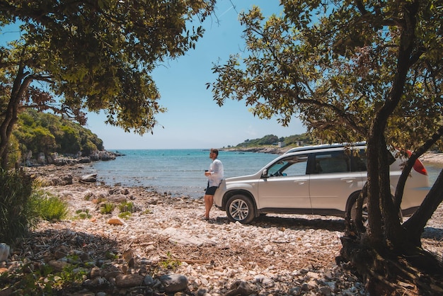 Hombre cerca de un coche todoterreno blanco en la playa de mar de verano