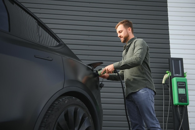 Foto un hombre se para cerca de una estación de carga y carga su coche eléctrico