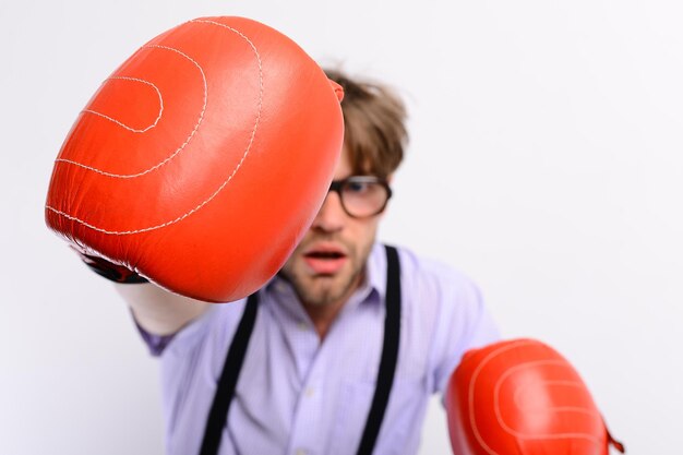 El hombre con cerdas y cara desenfocada usa guantes de boxeo. Competición y concepto de deporte inteligente. El tipo débil hace golpes y puñetazos, de cerca. Nerd con equipo de caja de cuero sobre fondo blanco.