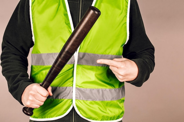 Hombre con un chaleco amarillo, un constructor o un manifestante con un bate de béisbol en las manos sobre un fondo gris