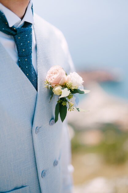 Un hombre con un chaleco azul, corbata azul y una delicada flor en el ojal con rosas y eucalipto closeup