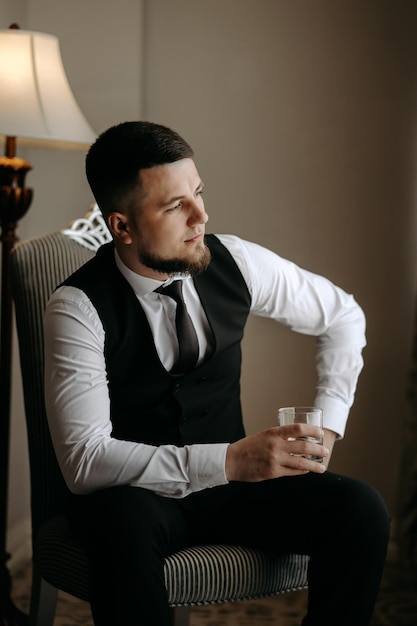 un hombre con un chaleco y corbata se sienta en una silla con un vaso de agua