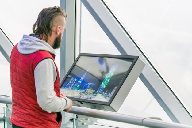 Hombre con un chaleco rojo mirando un monitor interactivo