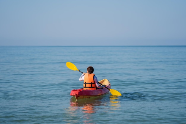 Hombre con chaleco salvavidas remando en un kayak en el mar