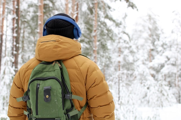 Un hombre con una chaqueta amarilla con una mochila en la espalda escucha con auriculares