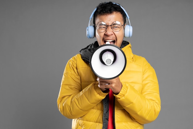 Hombre con chaqueta amarilla sobre pared gris gritando por un megáfono