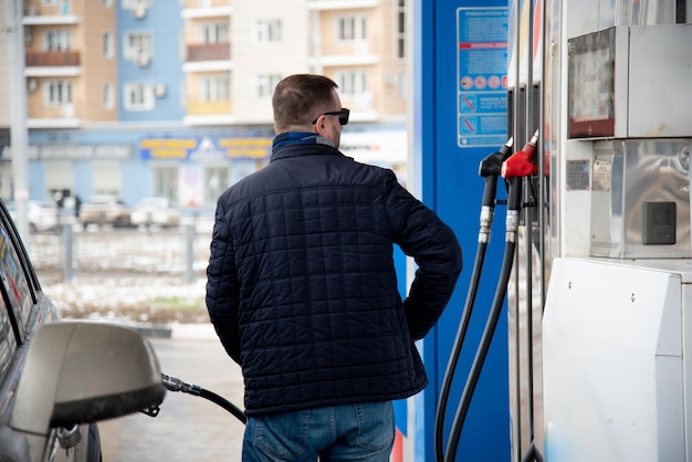 Un hombre con chaqueta azul y gafas oscuras en una gasolinera Llena el coche Gasolina Lifestile