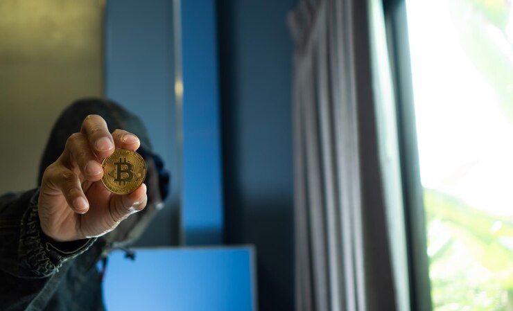 Foto hombre con chaqueta con capucha sosteniendo bitcoin mientras está sentado en el interior