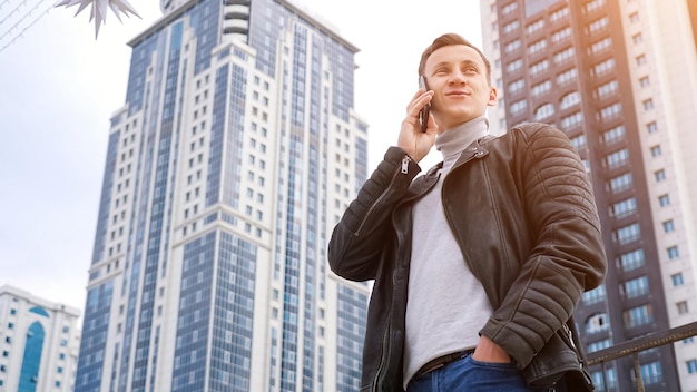 Hombre con una chaqueta de cuero hablando por teléfono con el telón de fondo de casas altas, copyspace