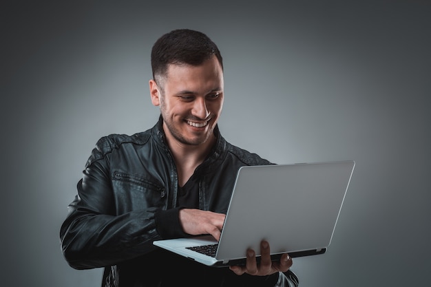 Hombre de chaqueta negra mirando portátil, media vuelta. Sosteniendo la computadora portátil abierta y trabajando. Emoción.