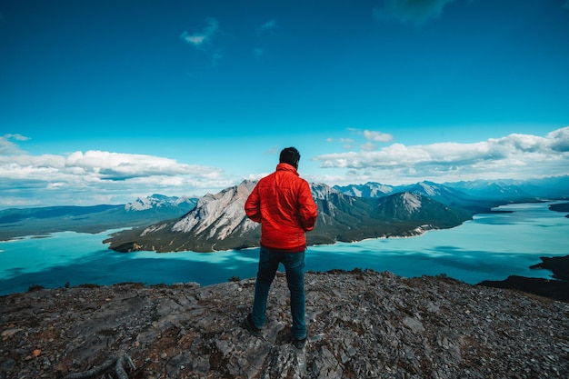 Foto un hombre con una chaqueta roja disfrutando de la vista desde un pico de montaña en alberta, canadá