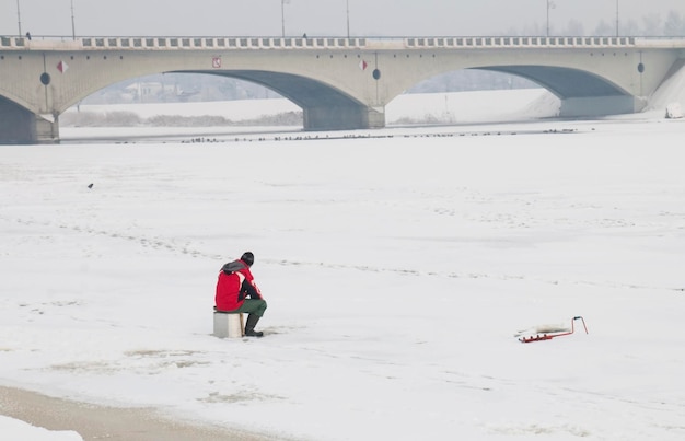 Un hombre en una chaqueta roja pescador pesca pesca en hielo