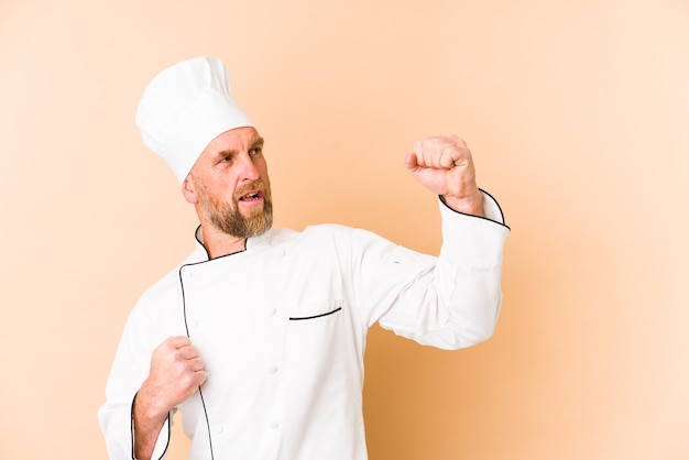 Hombre chef aislado en la pared beige levantando el puño después de una victoria, concepto ganador.