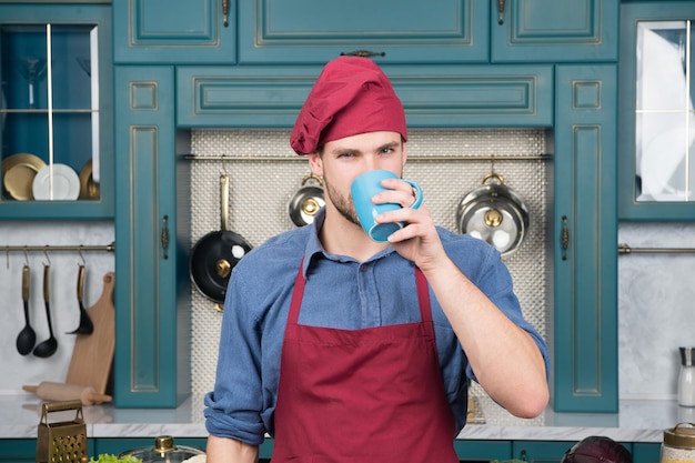 Hombre chef bebe té Hombre guapo sostiene una taza Barista experto y profesional que trabaja en un café bar o restaurante propietario de una pequeña empresa cocinero masculino en la cocina usa uniforme de personal