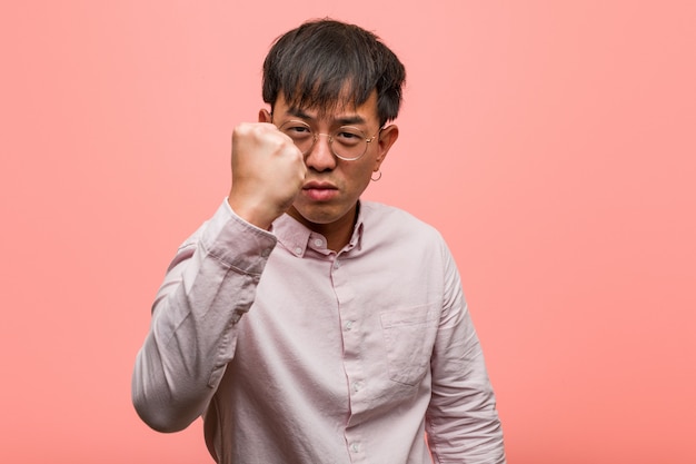 Hombre chino joven que muestra el puño al frente, expresión enojada