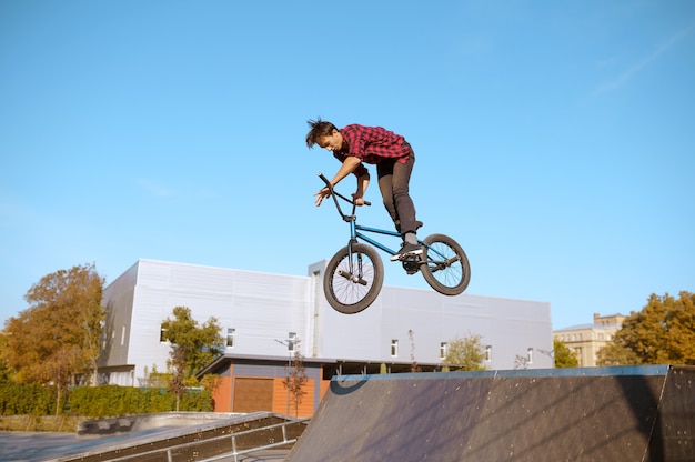 Hombre ciclista bmx salta en rampa, adolescente en entrenamiento en skatepark. Deporte extremo en bicicleta, ejercicio de ciclo peligroso, riesgo de montar en la calle, andar en bicicleta en el parque de verano