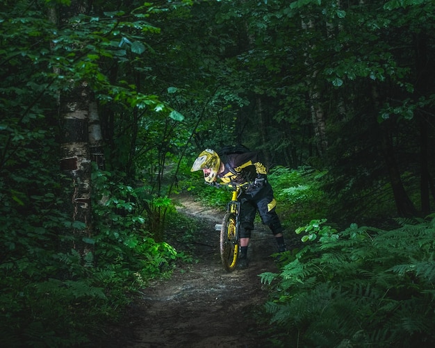 Hombre, ciclista con casco integral se para con la bicicleta de enduro amarilla en el bosque verde